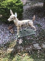 Full front-left view of cement deer sculpture on ground with bushes and gravel background
