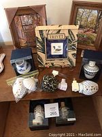 Photo of 3 framed nature art pieces with wooden stands and multiple boxed porcelain plug-in night lights arranged on a wooden surface.