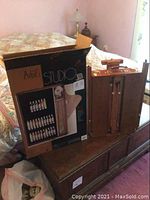 Photo shows the wooden folding floor easel standing open on a piece of furniture along with the original box packaging with images and listing of paint tubes inside.