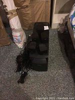 Full view of the Bose speaker system showing one large subwoofer, five small satellite speakers, and bundled cords placed on carpet.