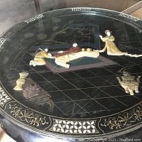 Close-up photo of the tabletop displaying the applied three-dimensional figures of Asian characters and objects along with the intricate gold and white inlaid border.