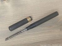 Safety razor fully extended showing razor head and comb-style blade guard attached to black textured fountain pen style capsule with gold band.