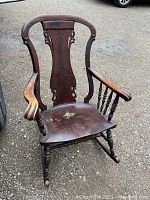 Front view of large wooden rocking chair showing carved backrest, curved armrests, and water stain on seat