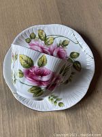 Close-up of the cup resting on the saucer showing the pink rambler rose floral pattern with green leaves and white ribbed textured porcelain with gold accents