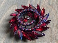 Top-down view of red rhinestone swirl brooch on wood surface.