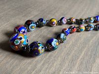 Close-up photo showing detailed Millefiori glass beads with floral patterns and metal spacers.