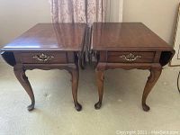 Pair of wooden drop leaf end tables side by side with leaves down, showing cabriole legs and single drawer with brass hardware.
