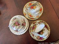 Photo showing three Royal Albert bone china tea cup trios with floral patterns and gold trim on a wooden surface.