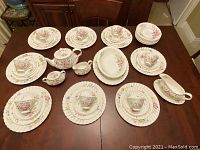 Full overview of eight place settings, teacups, saucers, serving pieces laid out on table