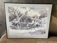 Framed print showing a rustic building in winter with snow and barren trees.
