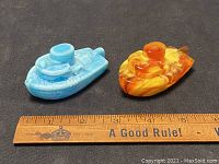 Pair of small glass tugboat figurines in blue and marbled orange with a ruler for scale showing approx. 3.5 inches length