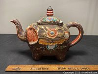 Full side view showing elephant trunk spout, detailed floral designs, and the teapot's brown color with multicolor accents.