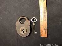 Rusty metal padlock with matching skeleton key placed next to a ruler showing size about 3 inches tall