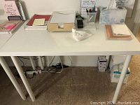 Front view of white Ikea table with various office supplies on top, showing dimensions and condition.