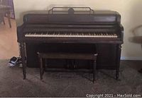 Full view of antique Wurlitzer upright piano with matching wooden stool showing dark finish with scratches.