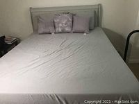 Full view of the queen bed frame made of light gray upholstery with fitted sheet and four decorative pillows in floral and solid patterns