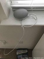 Google Home Mini smart speaker on white windowsill connected to power with visible charging cable and nearby business statistics book.