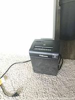 Photo showing the Fellowes small electric shredder plugged in on carpeted floor with control buttons visible on top and waste bin below.