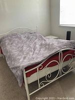 White metal queen platform bed frame with decorative curved headboard and footboard, shown with mattress and gray comforter.