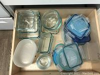 Multiple glass food storage containers grouped by shape with several plastic lids on the side showing sizes and locking mechanisms.