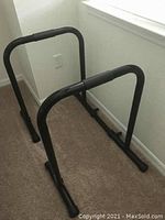 Photo showing the black metal dip station with padded grips and angled legs, placed on carpet near a window and power outlet.