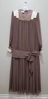 Front view of brown/taupe chiffon vintage 1980s Frank Usher drop waist dress with cream lace collar and cuffs, pleated bodice and skirt, sash tied at waist.