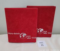 Two red binders with 'Münz-Briefe aus aller Welt' white text and globe graphic on the cover