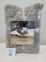Front photo of the oversized sage green throw blanket in clear plastic packaging showing the folded blanket and a printed label with a hammock beach scene and product details.