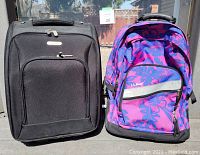 Front view of two carry-on suitcases side by side, black Travelon on left and purple floral L L Bean on right