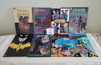 Seven DC Comics graphic novels with Batman and Superman characters visible on the cover, laid out on a white surface