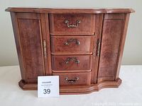 Front view of the wooden jewellery box with four central drawers and two side doors with brass handles, showing wood grain and finish.