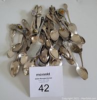 Lot of 39 assorted souvenir teaspoons from around the world stacked loosely showing various decorative handles and bowl shapes.