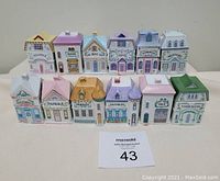 Front view of 12 Lenox ceramic spice jars shaped like houses, showing different spice names and colorful roofs.