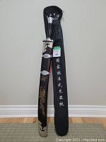 View of the sword in its hard sheath alongside the soft carrying case showing dragon and cloud designs on sheath and Chinese characters on case.