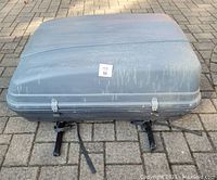 Closed grey Motomaster cartop carrier showing scratches and wear on the top surface, attached straps and mounting bars visible underneath.