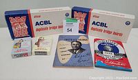 Two boxes of ACBL duplicate bridge boards and two vintage bridge books displayed with two decks of Audrey's codes cards.