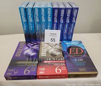 Twelve new sealed T-120 VHS tapes neatly arranged showing front packaging of all brands and grades.