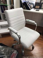 Front/right angled view showing white leather seat, backrest, padded armrests and chrome base with casters.