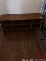 Wooden storage bench with eight cubbies visible from the front, standing on a wood floor.