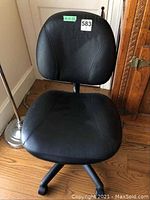 Black rolling office chair with visible adjustable back and seat bottom, faux leather upholstery, five caster wheels, placed on wood floor.