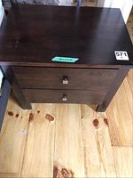Front view of one bedside table showing two drawers with square metal handles and surface wear.