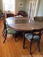 Full view of the oval dining table with four carved balloon back chairs, showing wood floor setting.