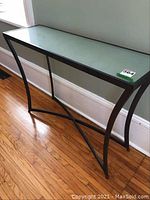 Full view of black metal hall table with frosted glass top showing overall design and structure against a wall.