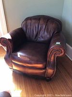 Front angle of brown leather club chair showing overall shape, upholstery and wooden base