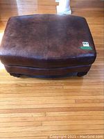 Top view of brown leather ottoman showing surface wear and scratches.
