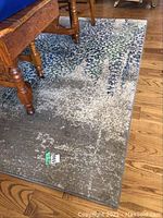 Photo showing part of the patterned area rug under wooden furniture on a hardwood floor, focused on the rug's edge and texture.