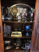 Silver platter and stemware arrangement on shelves including glassware, silver plated pieces, and pottery.