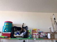 Photo showing coolers, picnic backpack with wine compartment, cutlery, cups, and water squirters arranged on green shelf.