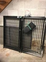 Two black wire mesh panels leaning against basement wall with attached zip plastic bag of hardware and rolled black tarp.