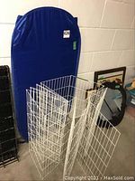 White metal wire pet enclosure panels arranged standing and folded against the wall next to the blue foldable mat.